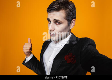 Photo de portrait homme zombie halloween costume classique sur le port et en tenant un miroir sur fond jaune isolé selfies Banque D'Images