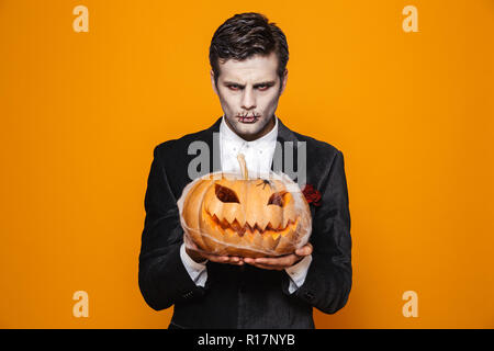 Photo de dead époux sur le port d'halloween costume classique et maquillage creepy holding carved pumpkin sur fond jaune isolé Banque D'Images