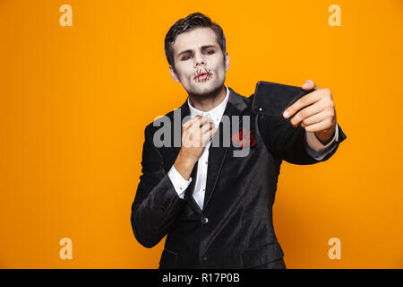 Handsome man zombie halloween avec le maquillage et en fonction de décisions isolées sur smartphone selfies sur orange Banque D'Images