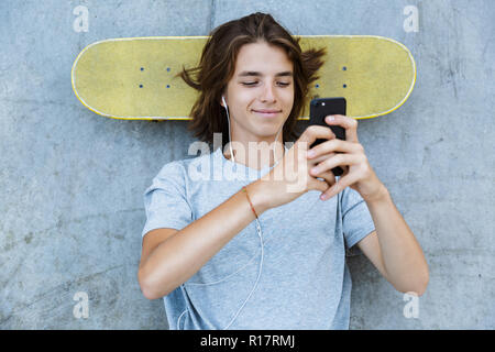 Vue de dessus d'un jeune garçon teenge joyeux passé du temps dans le skate park, portant sur une planche à roulettes à une rampe, écouter de la musique avec vos écouteurs Banque D'Images