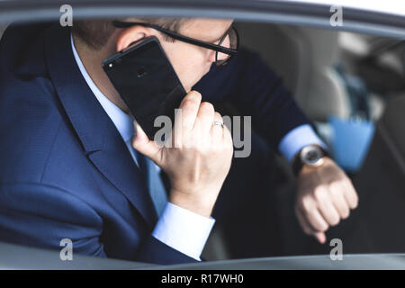 Jeune homme d'affaires réussi à parler au téléphone assis dans le siège arrière d'une voiture d'élite, des conférences et réunions d'affaires Banque D'Images