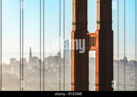 La ville de San Francisco, en Californie, est vue à travers les câbles de suspension et une tour de l'emblématique pont du Golden Gate sur un matin brumeux. Banque D'Images