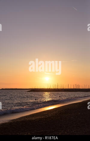 Photo verticale avec coucher de soleil sur la mer Méditerranée. Soleil est en arrière-plan derrière la jetée en pierre d'ancrage où plusieurs bateaux et navires. Ciel est clair wit Banque D'Images