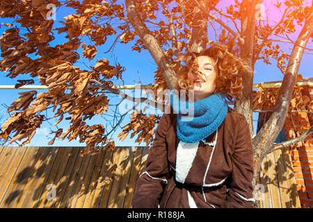 Style de mode portrait de jeune femme vêtue à la mode dans des vêtements élégants et souriant posant un arrière-plan de ion chêne avec des feuilles jaunies. po Banque D'Images