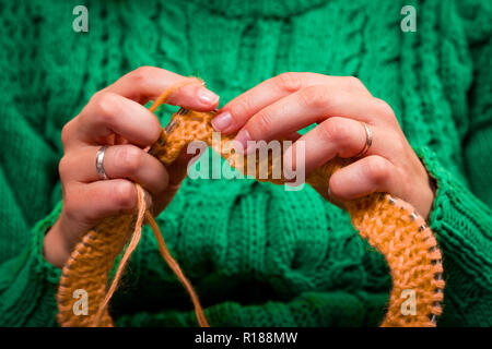 Close-up d'une belle femme à tricoter aiguilles à tricoter pull vert à partir d'un fil de laine naturelle un chapeau jaune, une femme montre comment tricoter correctl Banque D'Images