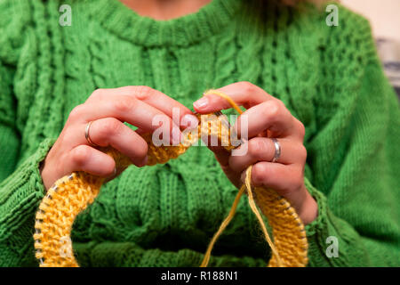 Close-up d'une belle femme à tricoter aiguilles à tricoter pull vert à partir d'un fil de laine naturelle un chapeau jaune, une femme montre comment tricoter correctl Banque D'Images