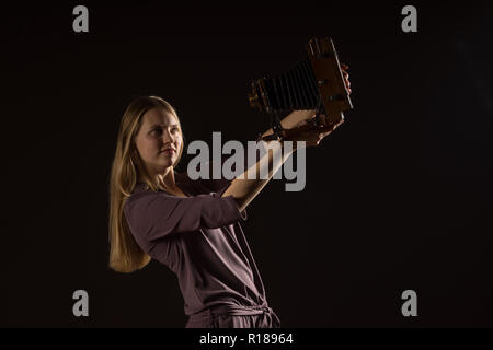 Portrait Portrait blanc modèle féminin. Belle fille, de longs cheveux blonds de prendre une photo avec l'appareil photo. Woman posing studio shot on a black backgrou Banque D'Images