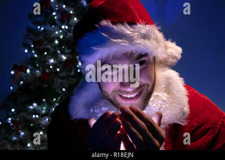Bonne recherche homme santa beach lumières dans ses mains in front of Christmas Tree Banque D'Images