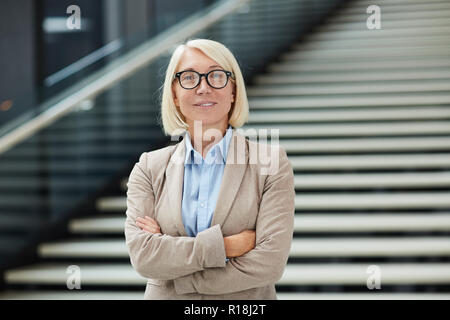 Blond businesswoman réussie en soirée et les lunettes croisant les bras sur la poitrine Banque D'Images