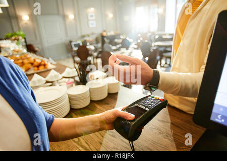 Main de jeune homme avec plus de poignet smartwatch sur machine de paiement détenus par adjoint de cafe Banque D'Images