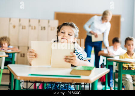 Adorable petite lycéenne livre lecture pendant la leçon Banque D'Images