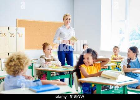 Beautiful smiling teacher marcher par classe d'enfants heureux Banque D'Images