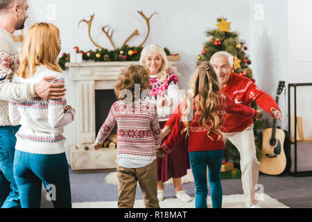 Vue arrière d'enfants qui courent à hug grands-parents pendant la veille de Noël à la maison Banque D'Images