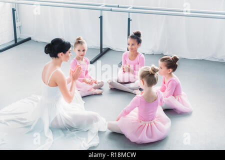 Portrait d'enfants en rose tutu jupes et jeune professeur de ballet assis ensemble dans l'école de ballet Banque D'Images