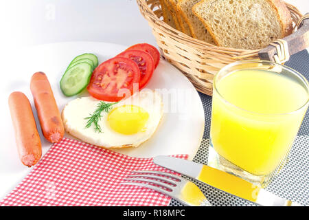 Le petit-déjeuner sur une plaque blanche sur un tableau noir et blanc. Œuf frit dans un cœur, saucisses, légumes frais concombres et tomates hachées, jus, sl Banque D'Images