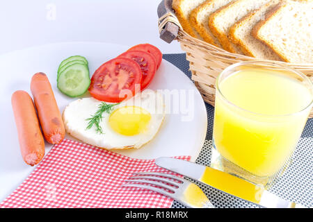 Le petit-déjeuner sur une plaque blanche sur un tableau noir et blanc. Œuf frit dans un cœur, saucisses, légumes frais concombres et tomates hachées, jus, sl Banque D'Images