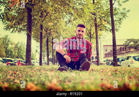 Un beau jeune homme en milieu urbain dans la ville européenne moderne, portant des jeans et chemise à carreaux rouge Banque D'Images