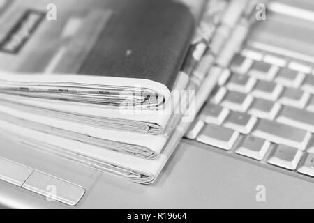 Journaux et ordinateur portable. Pile de quotidiens avec des news sur ordinateur. Avec Pages, des articles pliés et empilés sur le clavier de l'appareil électronique Banque D'Images