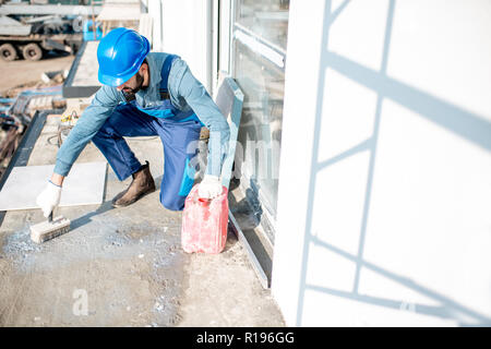 Workman en uniforme en béton d'amorçage à l'aide d'un pinceau pour les tuiles couché sur le balcon Banque D'Images