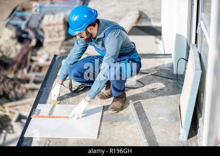 Workman en carreaux de céramique de fixation uniforme sur le balcon sur le site de construction Banque D'Images