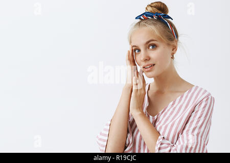 Jeune et jolie. Portrait de l'adjudication et douce belle femme blonde en blouse rose à rayures et bandeau, toucher le visage et le regard sur l'esprit de l'appareil photo Banque D'Images