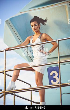 Un beau modèle féminin asiatique, métisse, posant sur un poste de sauveteur, une piscine en plein air concept éditorial de mode. Banque D'Images