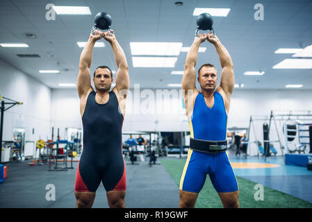 Deux poussoirs mâle levé sur leurs têtes, kettlebells entraînement de levage en salle de sport. Dans le sport ou d'entraînement d'haltérophilie club de remise en forme Banque D'Images