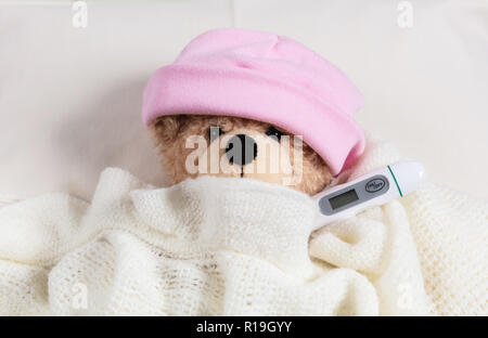 La fièvre, froid, concept de cheminée. Cute teddy girl avec un thermomètre dans le lit, recouvert d'une couverture chaude Banque D'Images