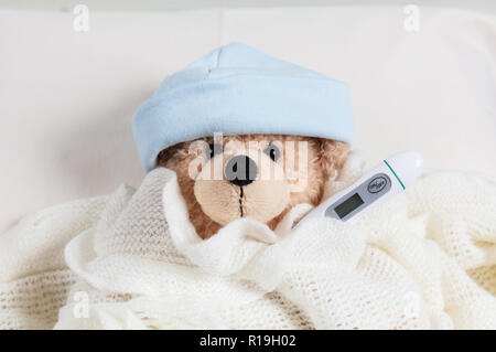 La fièvre, froid, concept de cheminée. Cute teddy boy avec un thermomètre dans le lit, recouvert d'une couverture chaude Banque D'Images