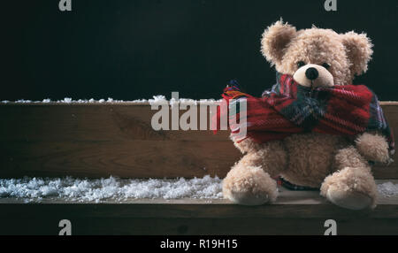 L'hiver, le froid, la solitude. Ours en peluche avec écharpe assis seul sur un banc de neige, bannière, copy space Banque D'Images