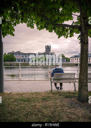 Man reading newspaper assis sur un banc en face de l'King John's Castle, Limerick, Irlande Banque D'Images