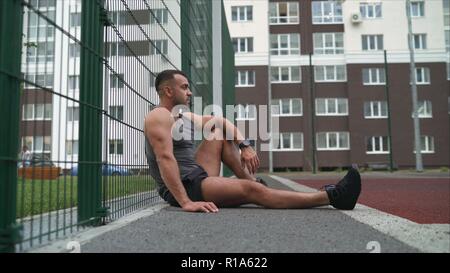 Man resting in health club. L'athlète est accroupis. Le mec est assis sur la cour. L'athlète est assis et se repose. Banque D'Images