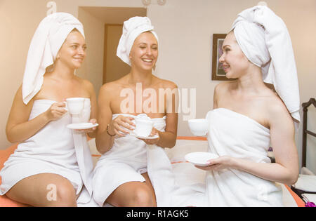 Trois jeunes filles mignonnes en blanc des peignoirs sont à boire le thé dans le salon spa. Reste après un sauna et un salon de procédures Banque D'Images