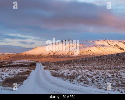 Une route couverte de neige menant vers une montagne ensoleillée en Islande Banque D'Images