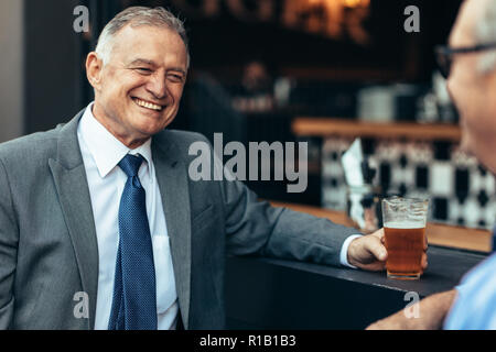 Souriant homme d'affaires senior avec un verre de bière parlant à un collègue au comptoir du bar après le travail. les gens d'affaires se détendent au bar après le travail. Banque D'Images