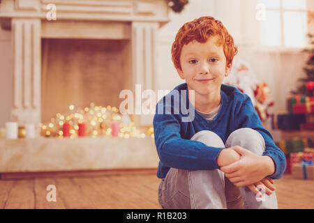 Gingembre optimiste garçon brun assis sur le plancher près de cheminée Banque D'Images