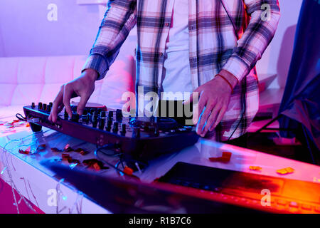 Tourné sans visage de l'homme en musique mixage DJ chemise sur console à table dans un éclairage ayant partie pour Nouvel An fête Banque D'Images