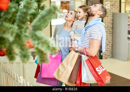 Les parents adultes contenu avec petite fille et les sacs en papier ayant les achats de Noël à Mall et à la recherche à tree Banque D'Images