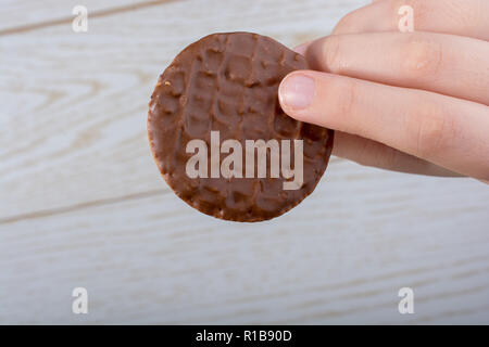 Main tenant un cookie recouvert de chocolat sur un fond de bois Banque D'Images