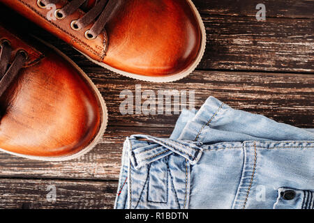 Les hommes en cuir marron bottes et jeans bleu foncé sur fond de bois Banque D'Images