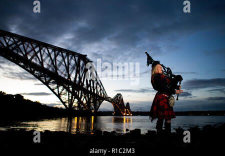 Louise Piper Marshall, vêtu d'un tartan rouge commémorative spéciale, joue Bataille, O'er, la lamentation écossais traditionnel joué à la fin de la bataille, à l'aube avec le Pont du Forth à North Queensferry sur le 100e anniversaire de la signature de l'Armistice qui a marqué la fin de la Première Guerre mondiale. Banque D'Images