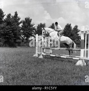 1967, un jeune garçon portant des culottes et un casque de saut à cheval une clôture à une piscine de concours complet, Wendover, Bucks, Banque D'Images