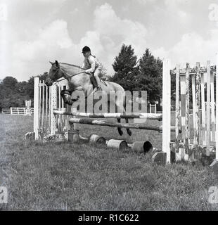 1967, Wendover, Bucks, une jeune fille sur un Cheval sautant une clôture à une piscine de concours complet. Banque D'Images