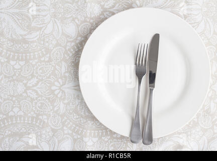 Le couteau et la fourchette sur l'assiette blanche sur l'élégante table à motifs blanc tissu - photo prise à la verticale Banque D'Images