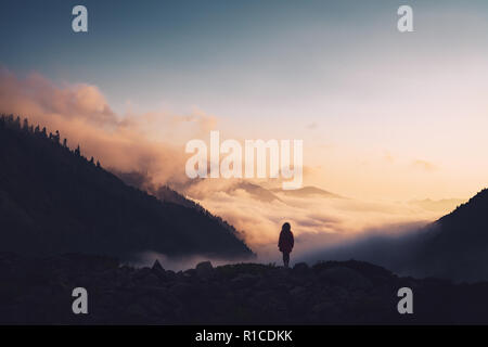 Silhouette d'une femme debout sur une crête, pour le coucher du soleil. Banque D'Images