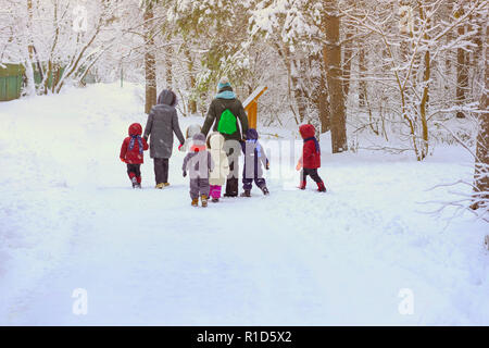 Groupe d'enfants avec litle méconnaissables des enseignants de la maternelle, de nouveau à nous, marcher main dans la main dans le parc de loisirs d'hiver, de neige, d'un mode de vie actif Banque D'Images