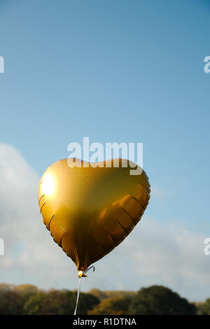 Un ballon en forme de coeur or voler contre un fond de ciel bleu, avec copie espace en mode portrait Banque D'Images