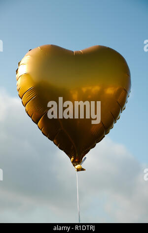 Un ballon en forme de coeur or voler contre un fond de ciel bleu Banque D'Images