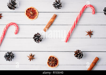 Schéma des bonbons de Noël, des pommes de pin et des oranges séchées sur fond de bois blanc. Décorations de Noël Banque D'Images