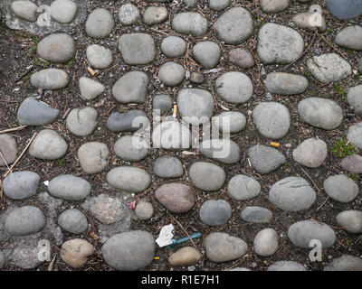 Vieux pavés ronds portés dans le sol sur une passerelle avec les mégots jetés épars dans une texture de fond plein cadre vue d'un Banque D'Images